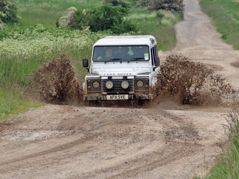 A white 4x4 Land Rover driving through a big puddle of mud