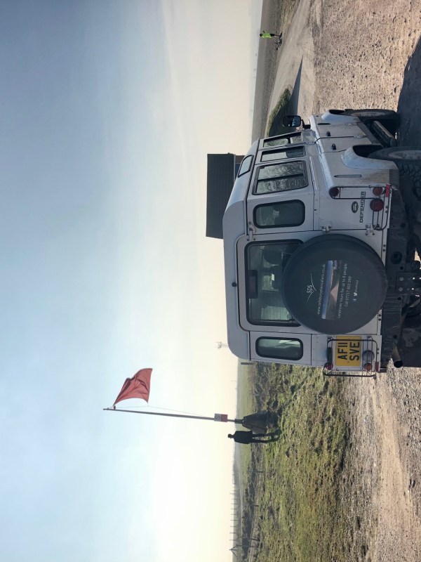 Picture of the back of a white 4x4 Land Rover on a pathway next to a field